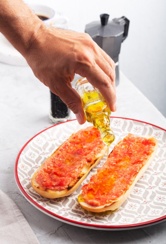 Hombre vertiendo aceite de oliva sobre una tostada de tomate